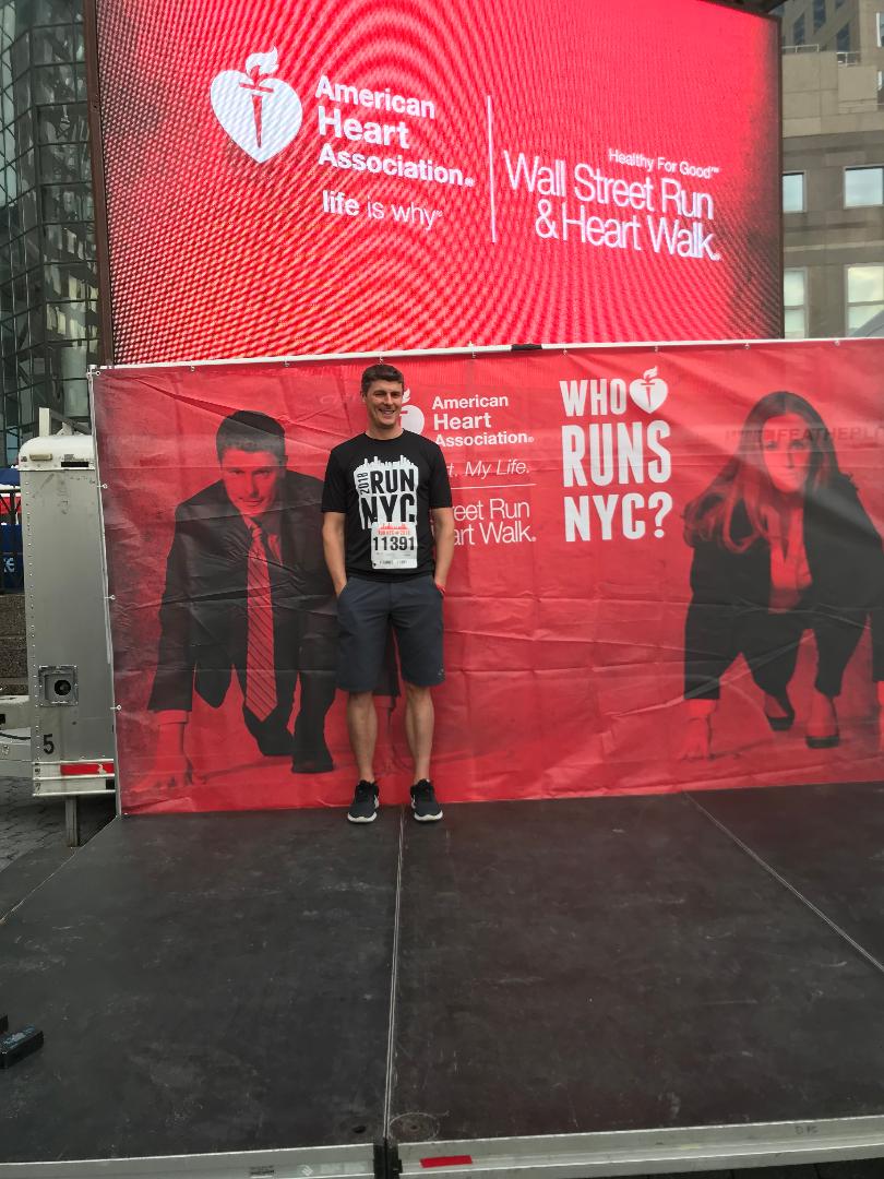 Scott standing beside his image on an American Heart Association Wall Street Run and Heart Walk campaign banner